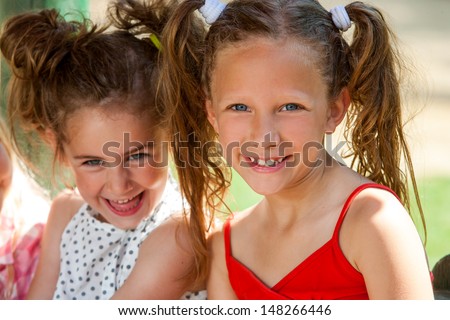 Close up portrait of two smiling pony tailed girls together outdoors.
