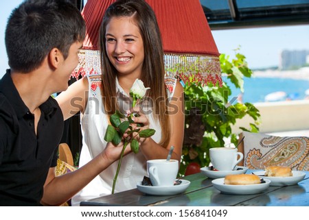 Young man giving flower to girl at coffee date.