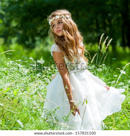 Cute girl holding white dress in green field.