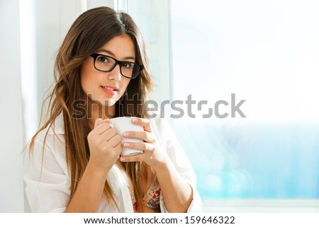 Close Up Portrait Of Cute Girl With Coffee Mug Next To Window With Sea View.