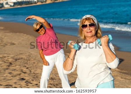 Two golden age women working out together on beach.
