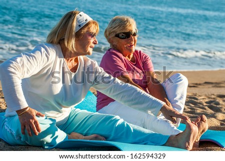 Close up portrait of two golden age women doing stretching exercises together on beach.