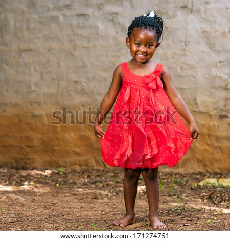 Full length portrait of cute african girl showing red dress outdoors.
