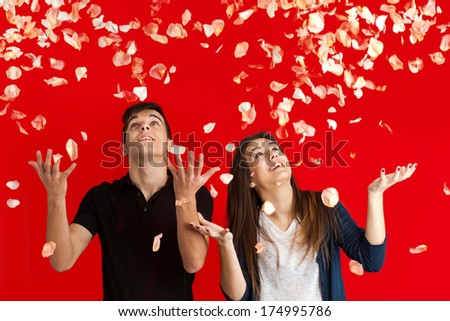 Couple with arms raised having fun throwing rose petals over red background.