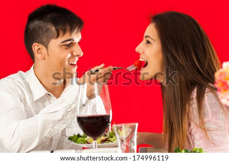 Fun Portrait Of Young Man Feeding Girlfriend At Romantic Dinner.