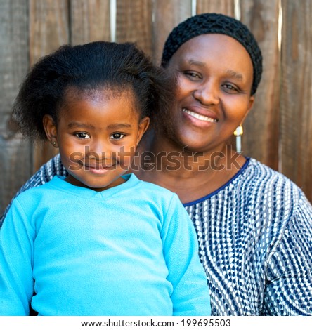 Portrait of African mom and daughter against wooden fence.