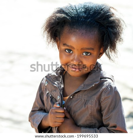 Portrait of Little African girl in brown jacket outdoors.