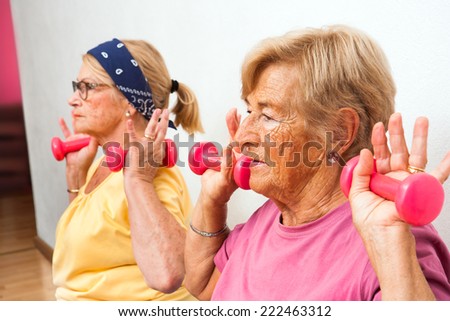 Close up portrait of two senior women doing exercise with weights in health club.