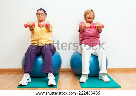 Portrait of Two elderly women doing muscle exercises with weights in gym.