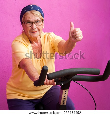 Fit senior woman doing thumbs up on at spinning session in gym.