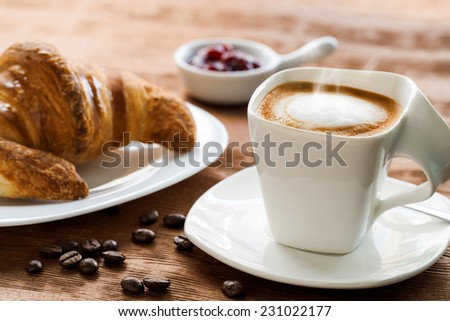 Extreme close up of Creamy coffee on wooden table with croissant in background.