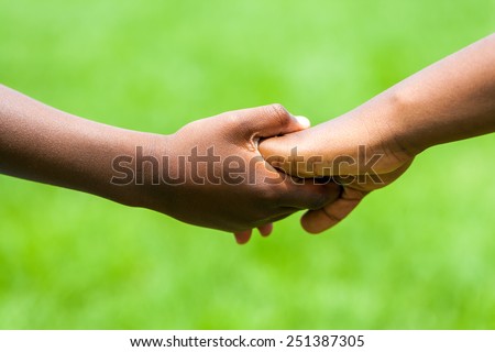 Extreme close up detail of African kids holding hands against green outdoor background.