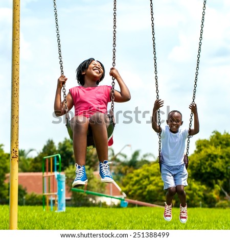 Action portrait of African kids having fun swinging in park.Out of focus houses in background.