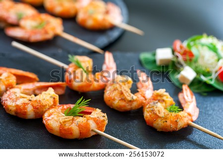 Macro close up of catering shrimp brochettes grilled with herbs. Out of focus salad in background.