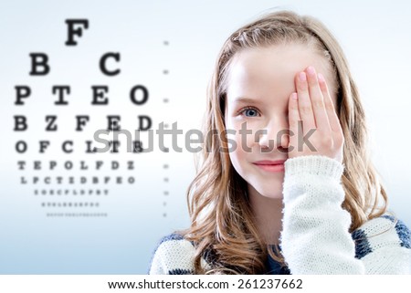 Close up portrait of girl reviewing eyesight closing eye with hand.Out of focus test chart in background.