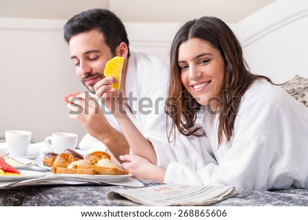 Close up portrait of couple having breakfast together on bed in hotel room.Couple wearing bathrobes.