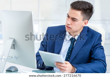 Close up portrait of young Businessman synchronizing digital tablet with computer. Young man sharing information between computer and digital tablet at desk in office.