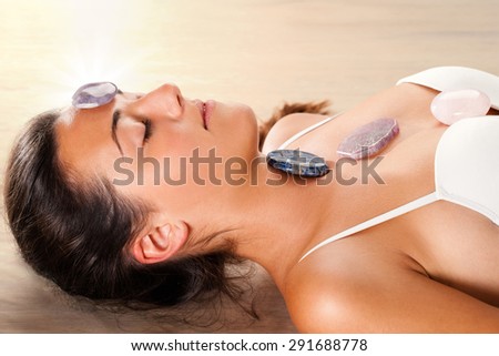 Close up of attractive young woman meditating with eyes closed. Precious gemstones on top of forehead and chest.