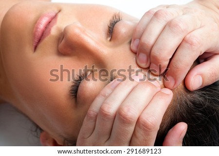 Macro close up face shot of young woman receiving massage. Therapist hand doing manipulative treatment on forehead.