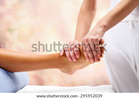 Osteopath doing reflexology massage on female foot against colorful background.