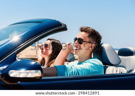Portrait of attractive young man driving with girlfriend in blue cabriolet.