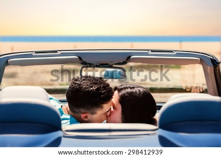 Portrait of young couple kissing in convertible. Rear view of couple in car next to beach.