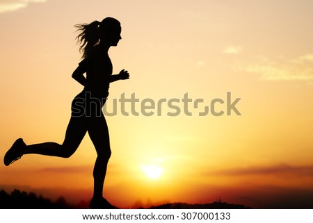 Close up action Silhouette of female jogger at sunset.Girl backlit against intense orange sky.