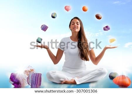 Full length portrait of young woman dressed in white doing yoga with precious gemstones.Conceptual image with colorful gemstones floating around girl.