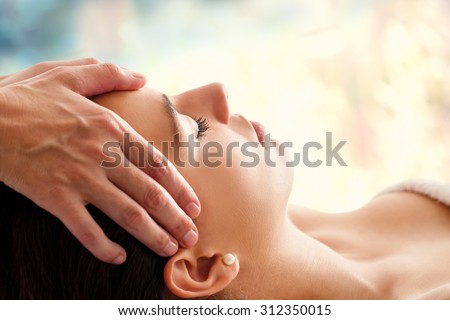 Close up head portrait of young woman having facial massage in spa. Therapist doing head massage  against colorful background.