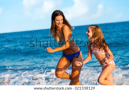 Action portrait of two Young girls having great time on beach.\
Girls running and splashing water.