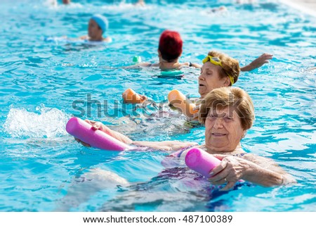 Close up portrait of senior woman doing body exercise with friends at aqua gym session in outdoor pool.