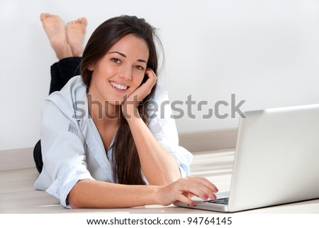 Portrait of young attractive woman laying on floor with laptop.