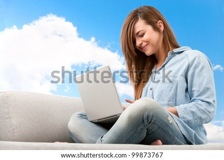 Young attractive woman sitting on couch with laptop.Blue sky background.