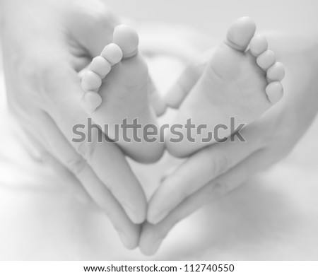 mother holds a newborn baby\'s feet, shape like a heart, black and white