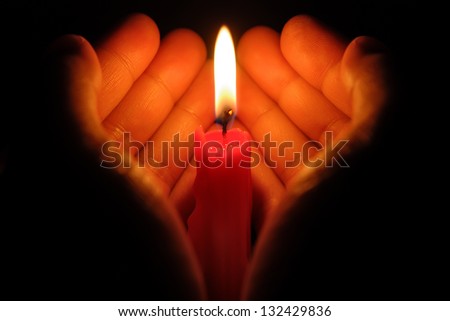hands holding a burning candle in dark