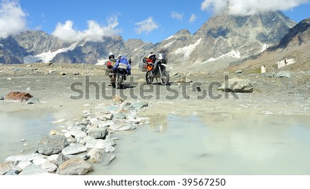 Two motorbikes parked on the shores of a small glacier lake in the Italian Alps near the Matterhorn peak