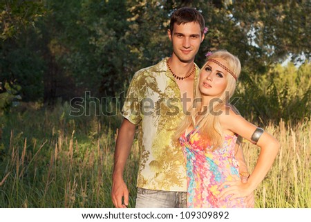 young man and beautiful blonde with flowers in hair stand in forest. style of hippie