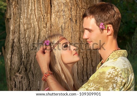 young man decorates hair of beautiful blonde with flower. style of hippie
