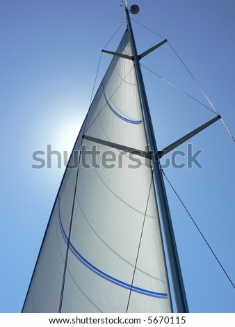 A view looking upwards at the mast, sail and rigging of a private yacht underway. Vertical perspective.
