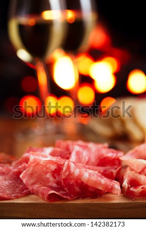 Platter of serrano jamon Cured Meat with cozy fireplace and wine background
