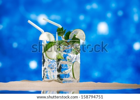mojito cocktail with ice, rum, lime and mint   in a  glass  on beach sand and  blue stars background