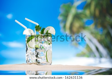 mojito cocktail with ice, rum, lime and mint   in a  glass  on beach sand and  blue stars background