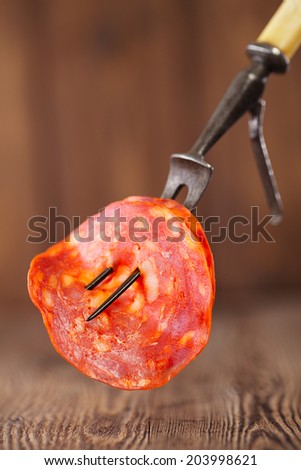 slice of sausage chorizo on meat fork and wooden backdrop
