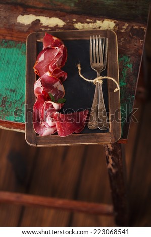 Cured Meat and vintage forks on textured Chalkboard and old wooden stool background