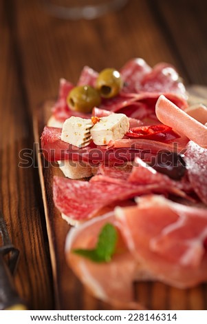 antipasti Platter of Cured Meat,   jamon, olives, sausage, salami,  ciabatta and white wine glasses on textured wooden table