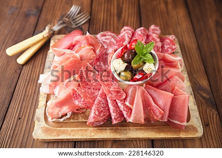 antipasti Platter of Cured Meat,   jamon, olives, sausage, salami,  ciabatta and white wine glasses on textured wooden table