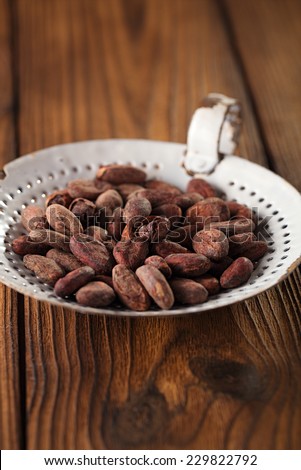 roasted cocoa chocolate beans in old enamel sieve, textured  wooden background