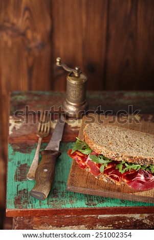 cured meat sandwich with seeded bread on old wooden table, shallow dof