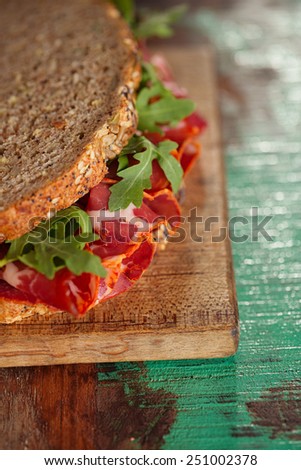 cured meat sandwich with seeded bread on old wooden table, shallow dof