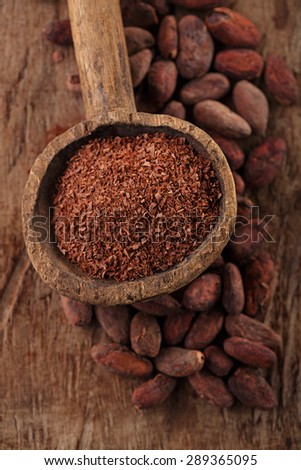 grated dark chocolate in old wooden spoon on roasted cocoa chocolate beans background